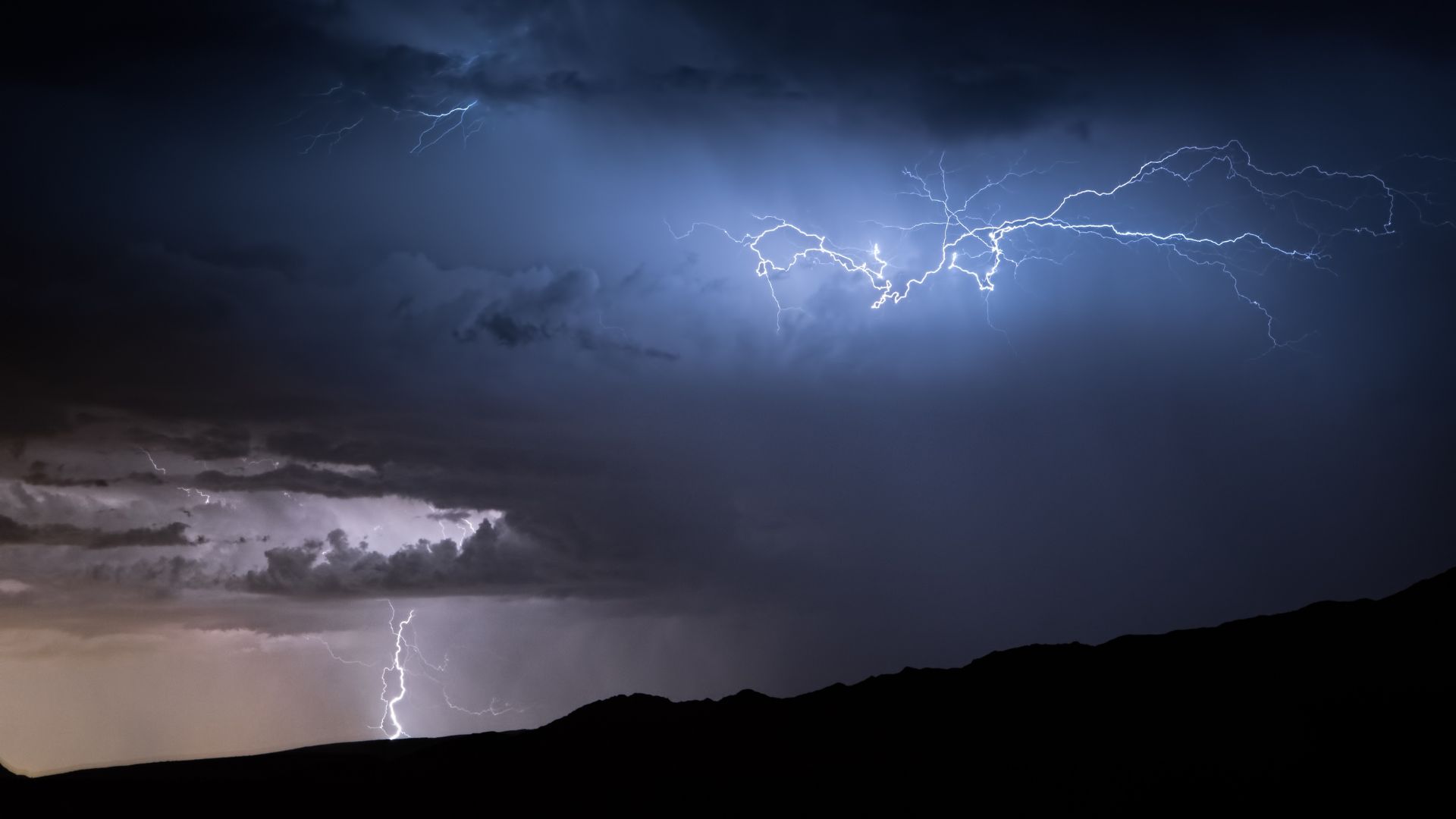 roof-restoration A night scene with lightning bolts flashing across a dark, cloudy sky above silhouetted hills.