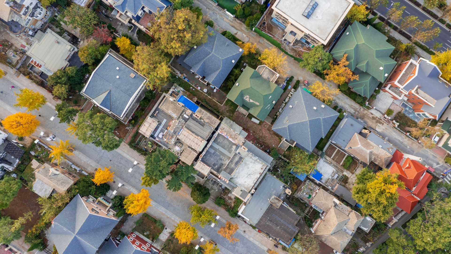 An aerial view of a residential neighborhood showing multiple houses with roofs in a variety of materials, including shingle, metal, and concrete.